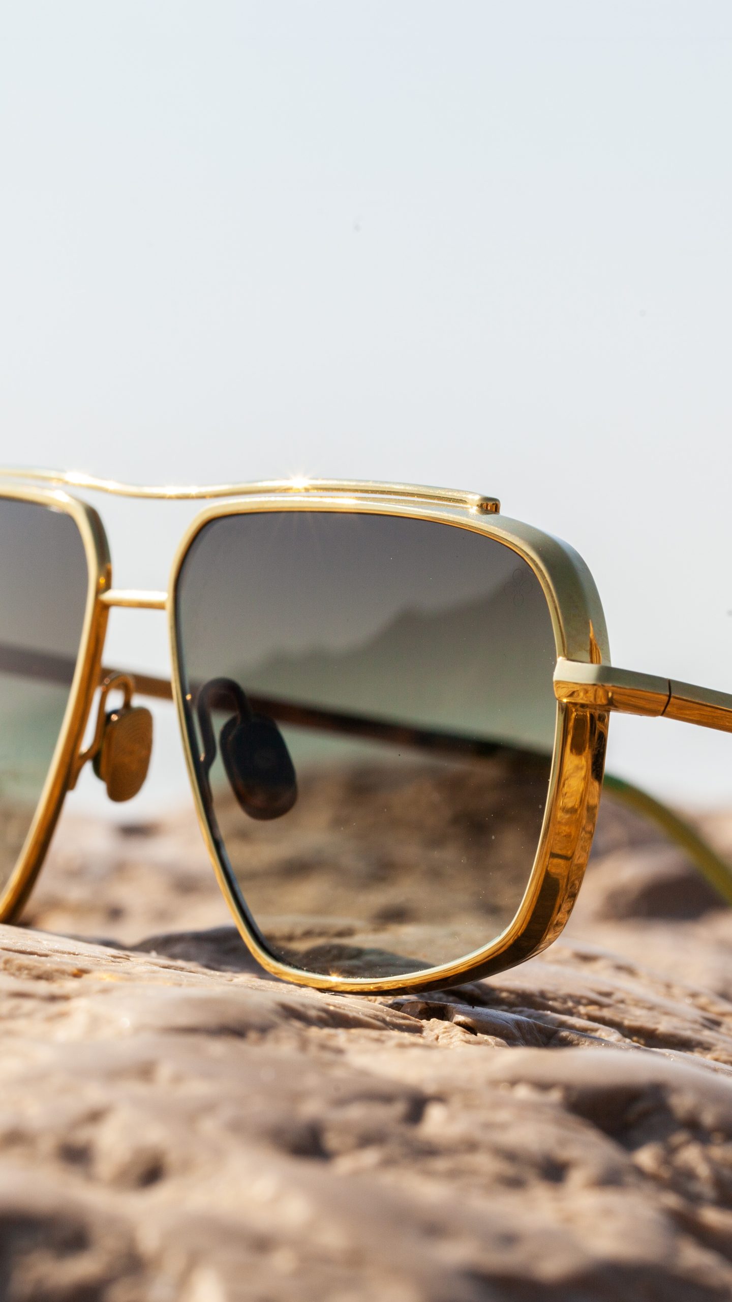 Lingot block titanium frame in 18K gold with green lenses, resting on Mediterranean rock